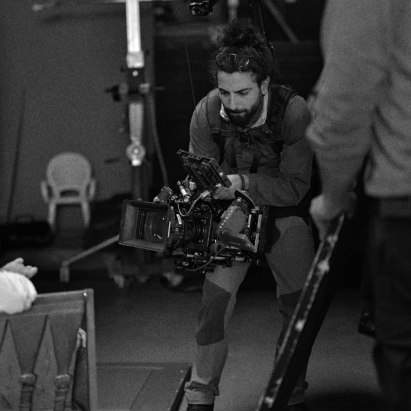 A black and white image capturing a filmmaker with a camera indoors.